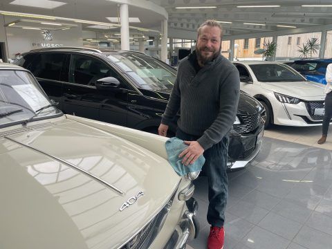 Ein Mann steht neben einem Auto in einem Ausstellungsraum.