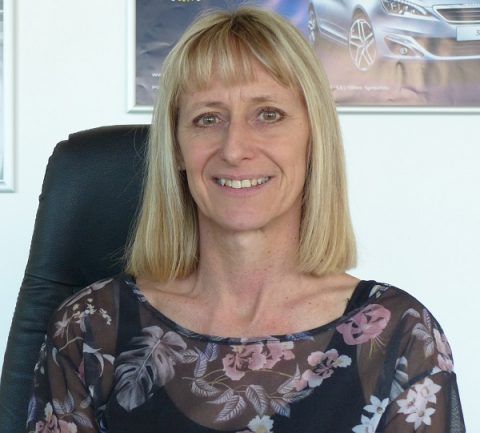 Eine Frau sitzt auf einem Stuhl, an der Wand hinter ihr hängt das Bild eines Autos.