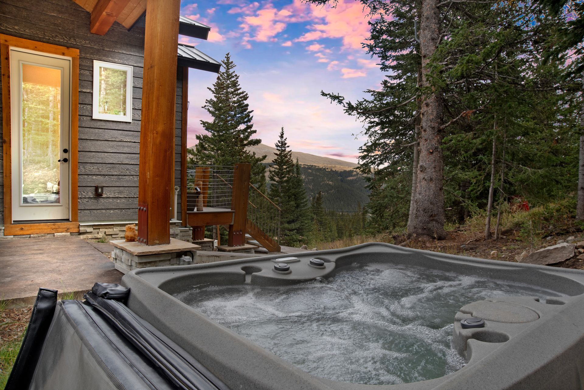 Hot tub on a wooden deck next to a cabin, overlooking a mountain vista at sunset.