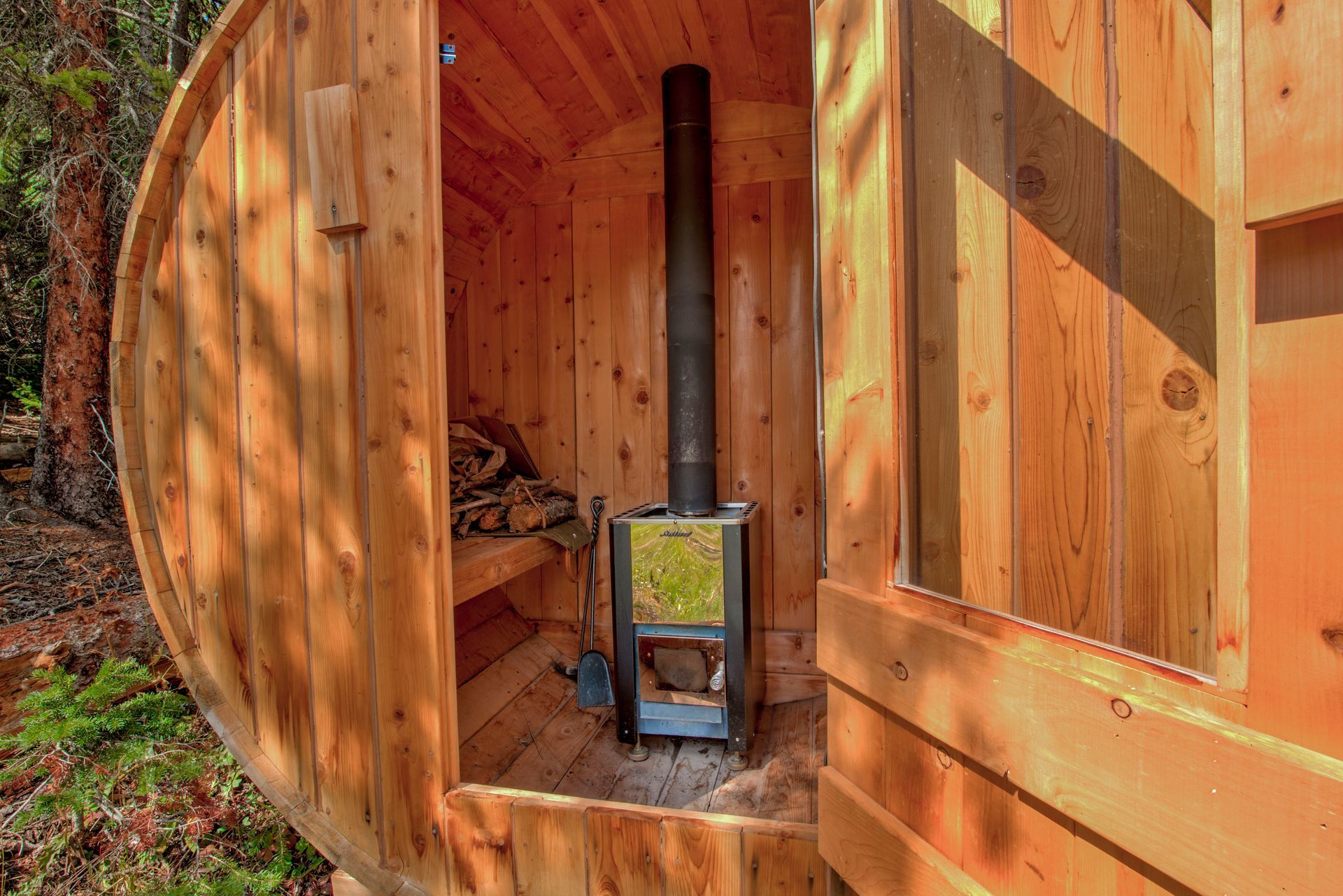 Wooden barrel sauna interior with a wood-burning stove and a bench.