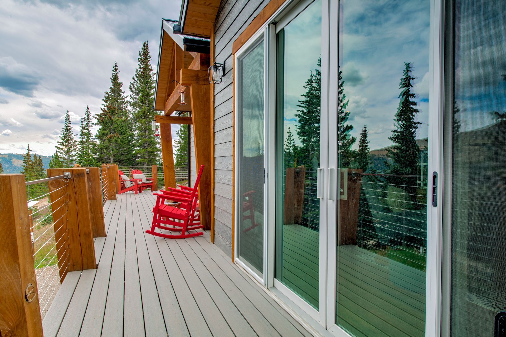 Wooden deck with red rocking chairs, overlooking a mountain view, next to a cabin with sliding glass doors.