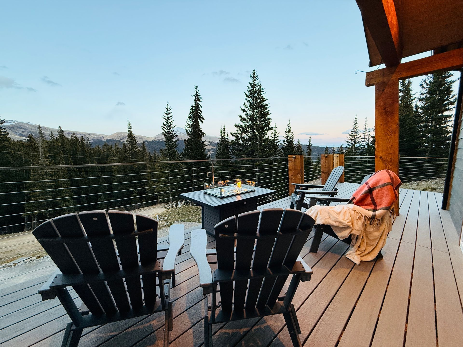 Patio with Adirondack chairs, fire pit table, and mountain view at dusk