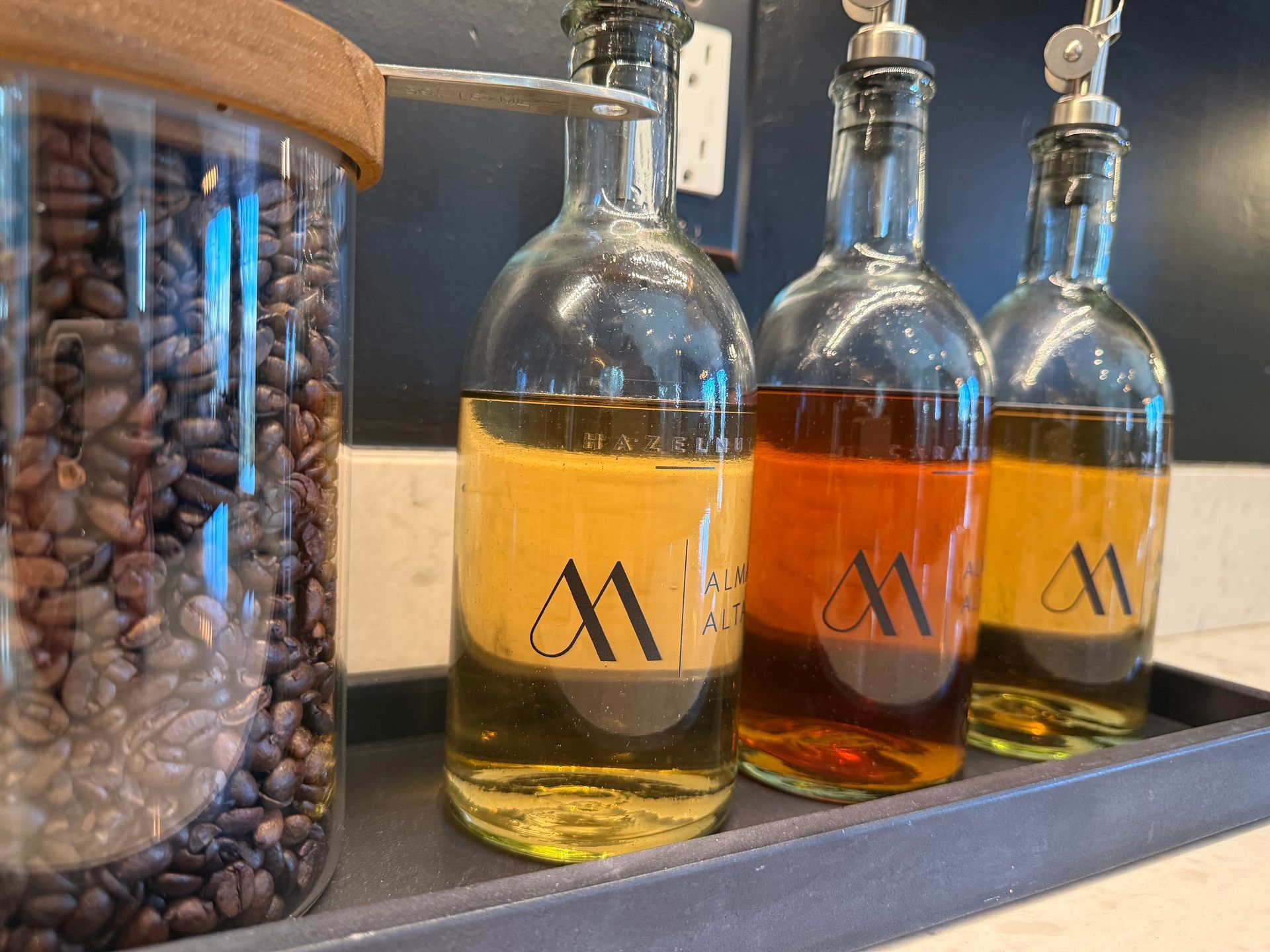 Glass bottles of liquid condiments and a jar of coffee beans on a tray.