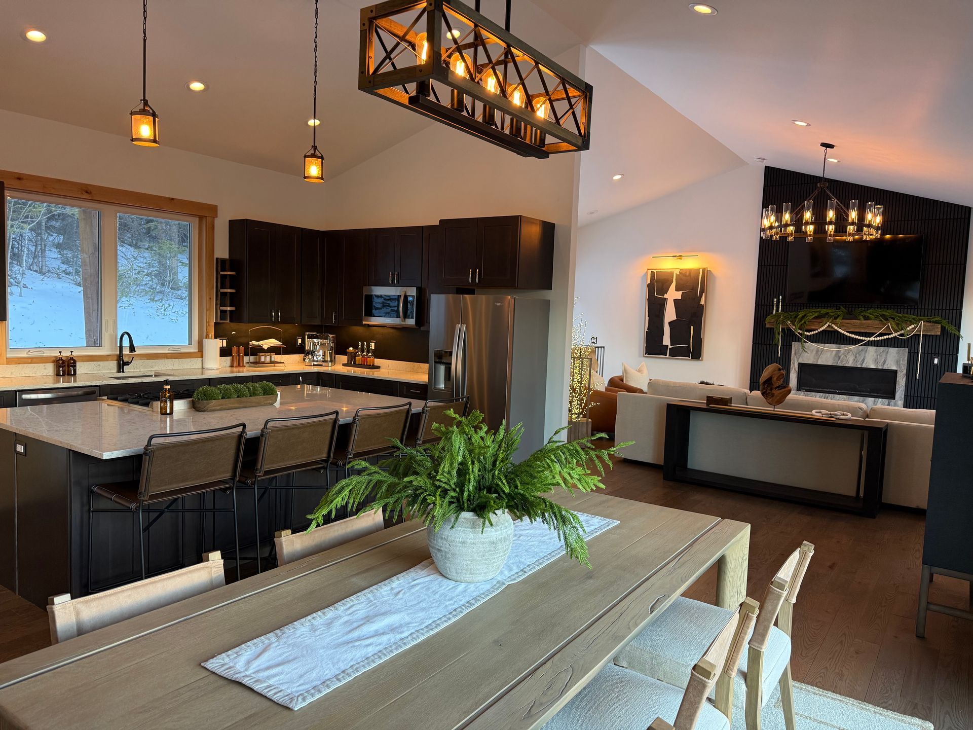 Modern kitchen and dining area with dark cabinets, a large island, and a long wooden table.