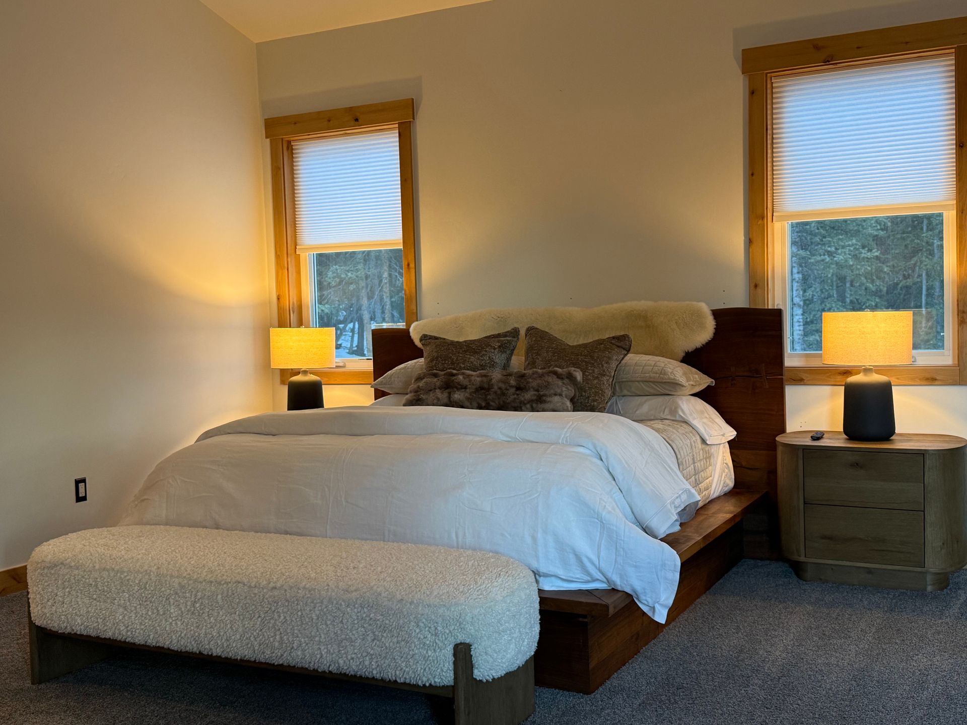 Bedroom with bed, bench, two nightstands, two windows, and lamps.
