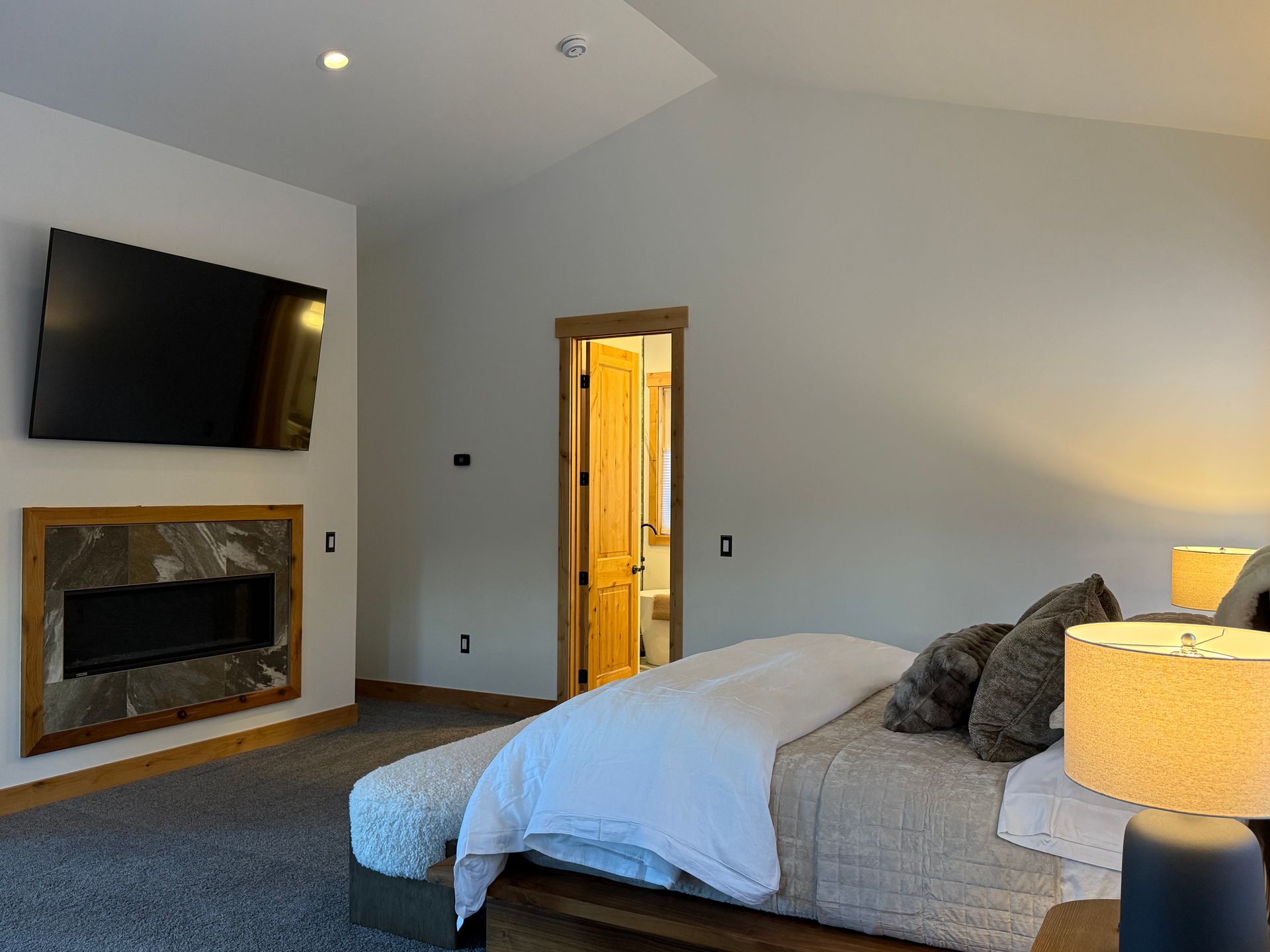 Bedroom with a TV over a fireplace, bed, and doorway to a bathroom.