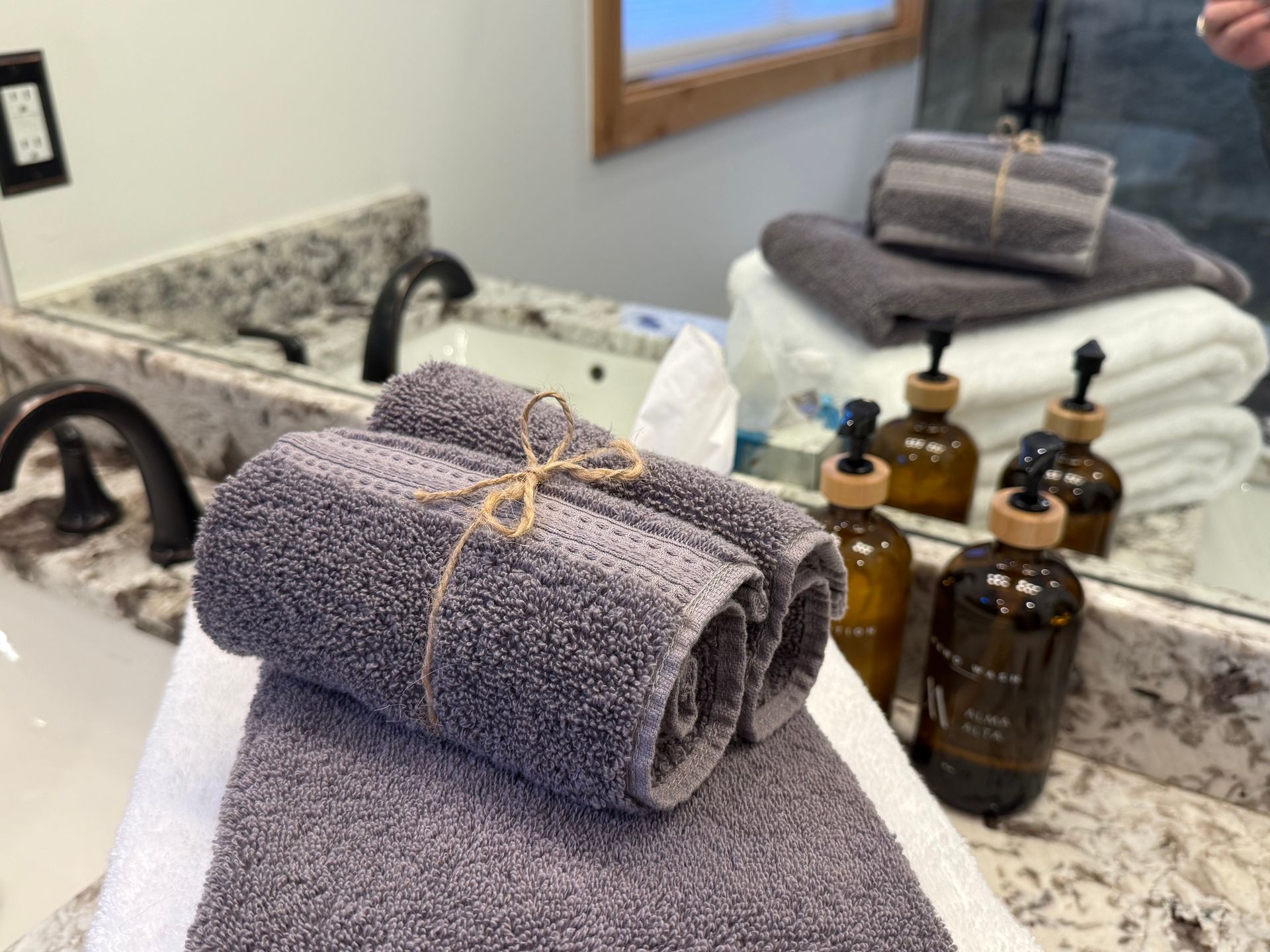 Bathroom vanity with rolled gray towels tied with twine, soaps, and stacks of towels.