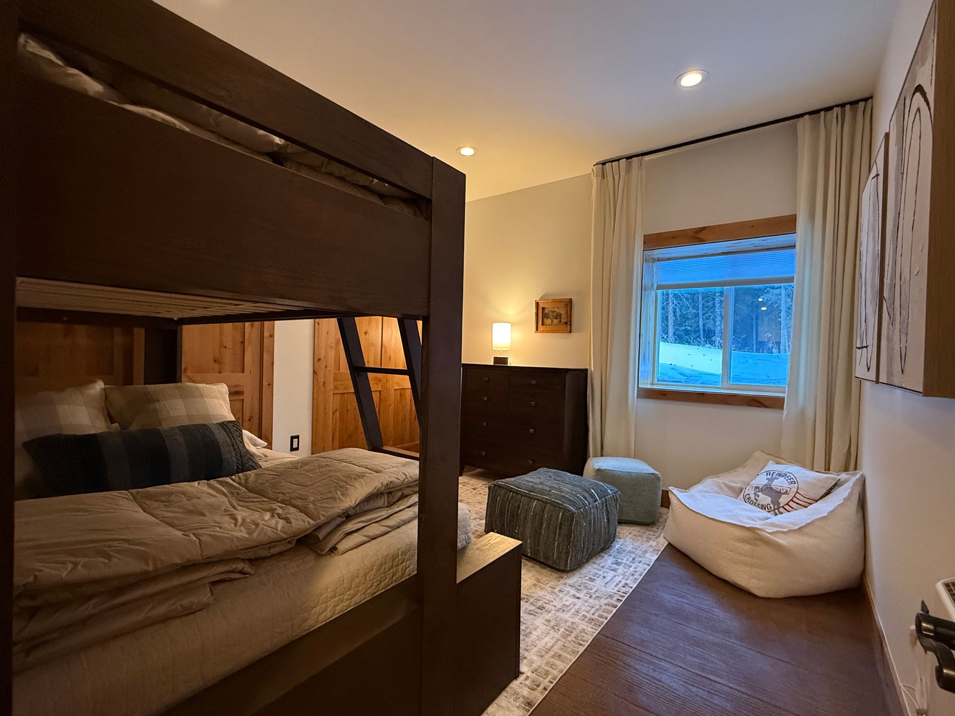 Bedroom with bunk bed, dresser, window, and small seating.