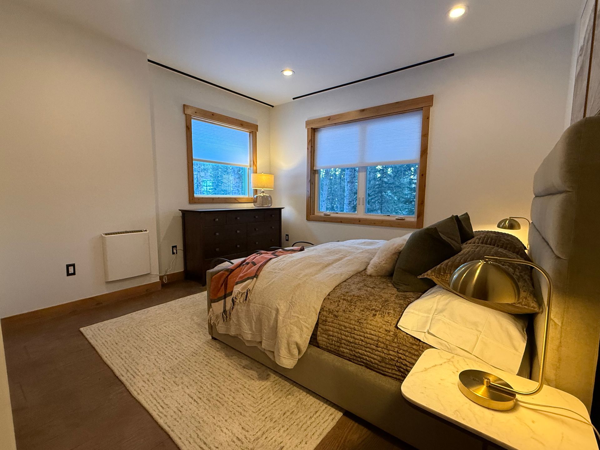 Bedroom with bed, windows, and chest of drawers. Neutral tones with a light rug on the floor.