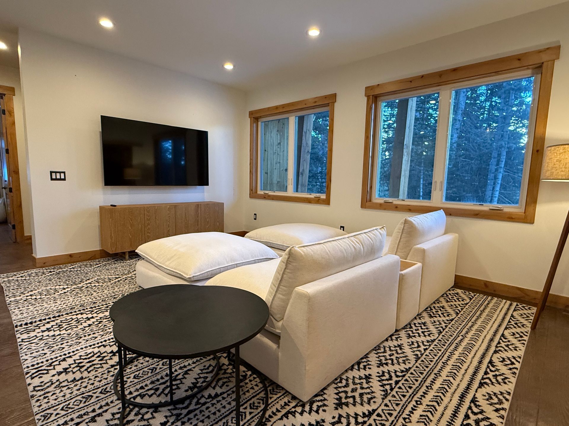 Living room with white sofa, black patterned rug, TV on wall, windows, and small black table.