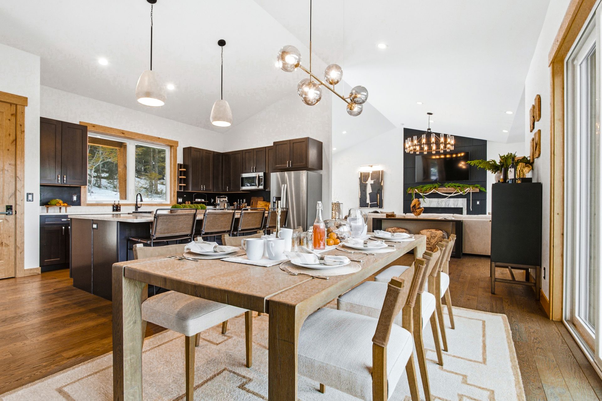 A brightly lit open-concept kitchen and dining area featuring a wooden table, chairs, and modern lighting fixtures.