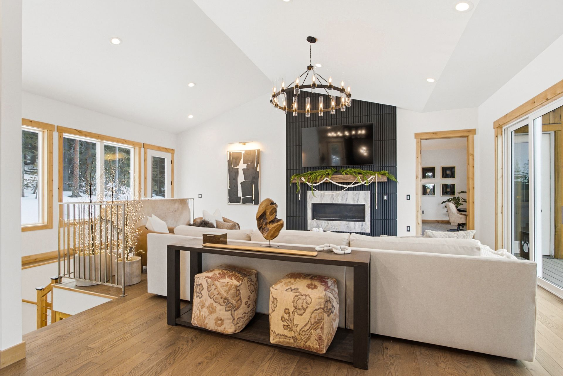 A bright living room featuring a light-colored sofa, patterned ottomans, a central fireplace, and large windows.