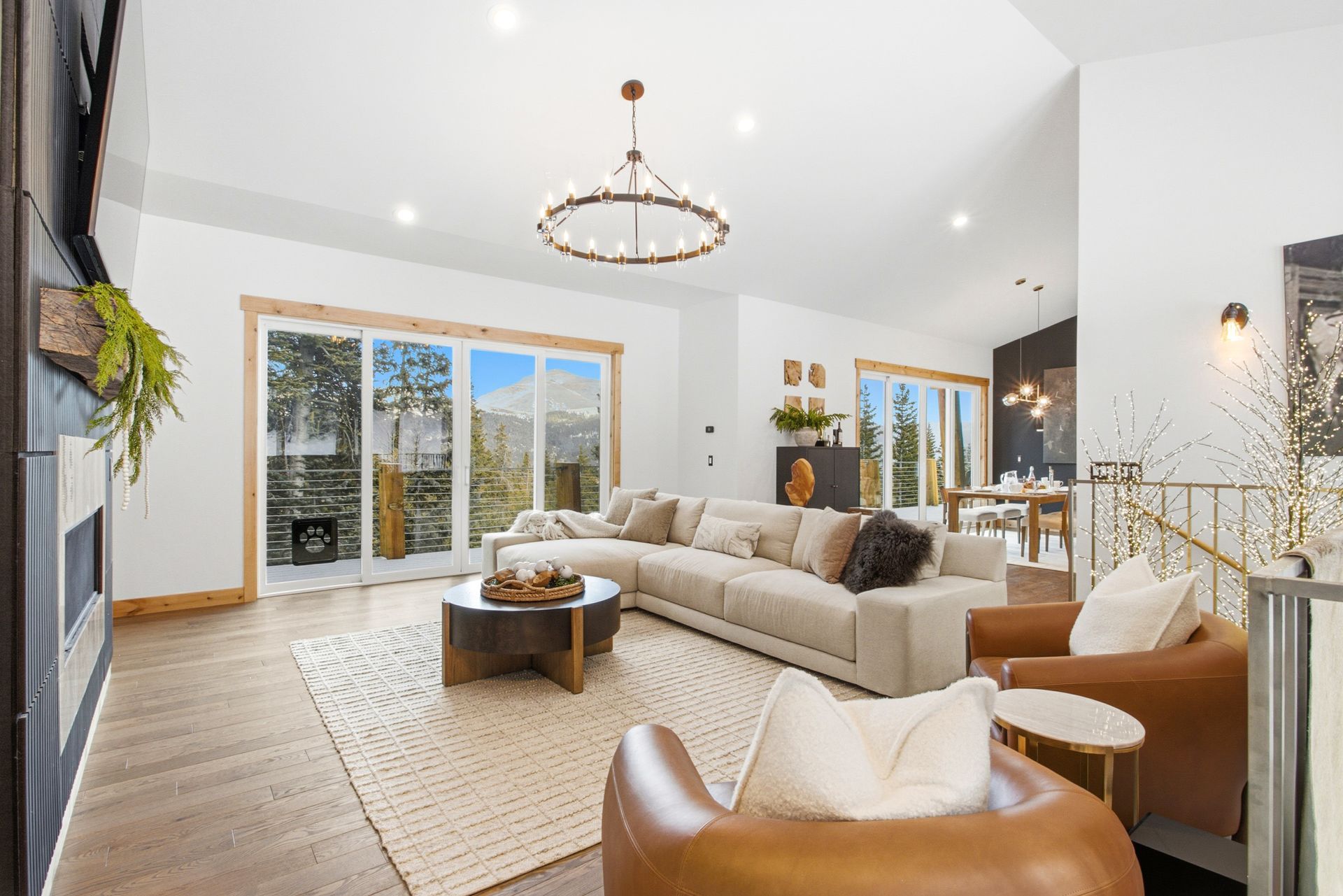 A spacious, modern living room with a cream sectional sofa, two leather armchairs, a rug, and large glass sliding doors.