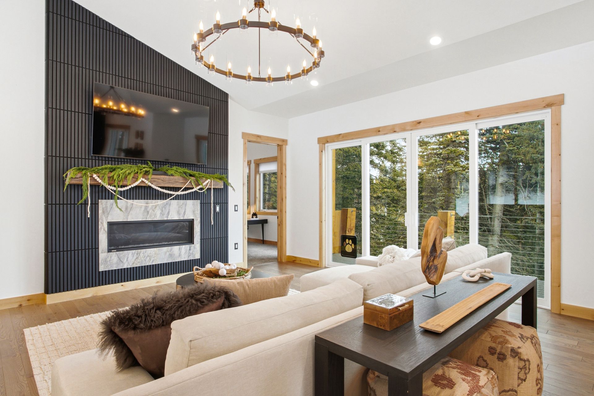 A modern living room with a fireplace, a mounted TV on a dark slat wall, a white sofa, and large sliding glass doors.