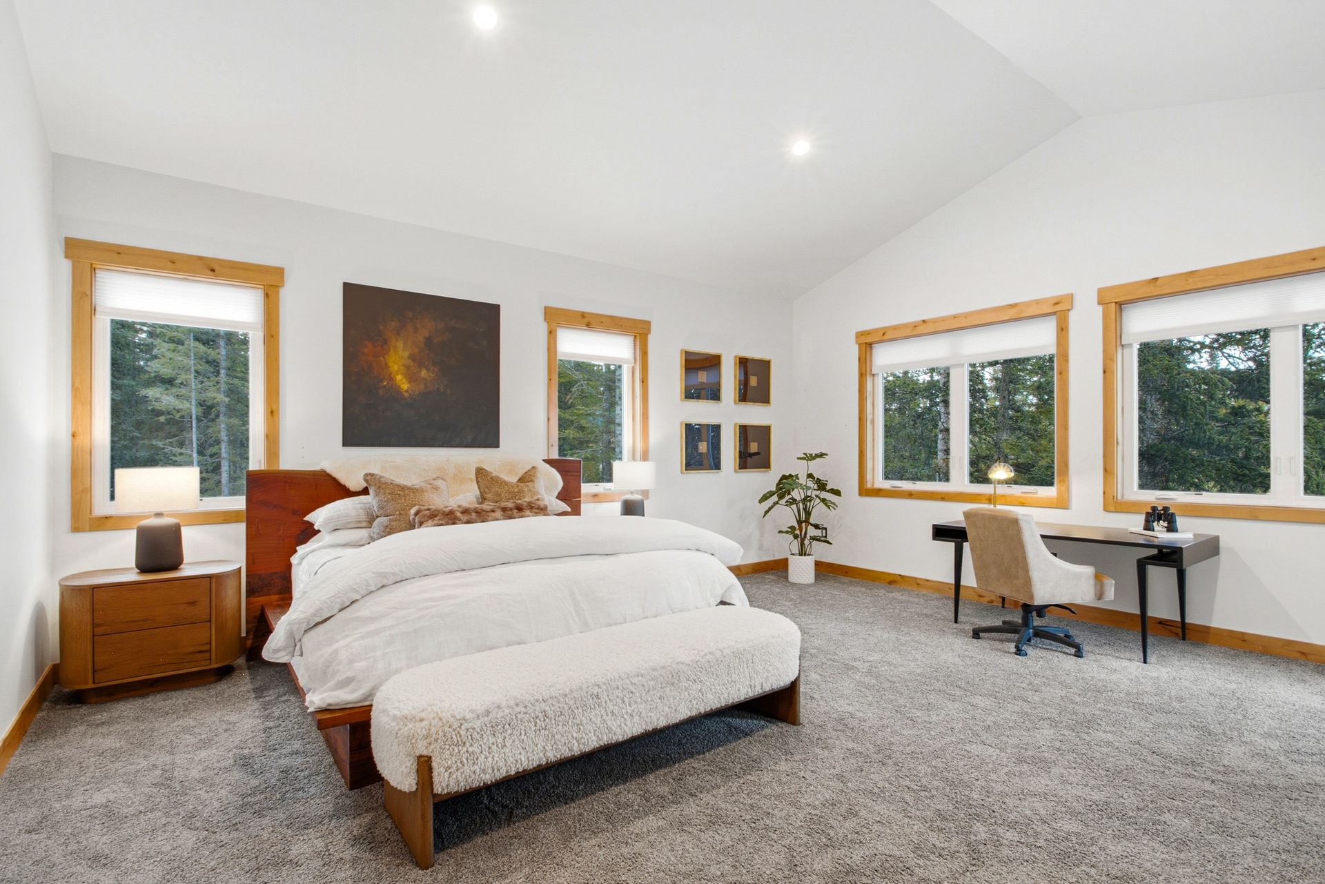 Bright bedroom with a large bed, white walls, wood accents, windows, and a small desk by the window