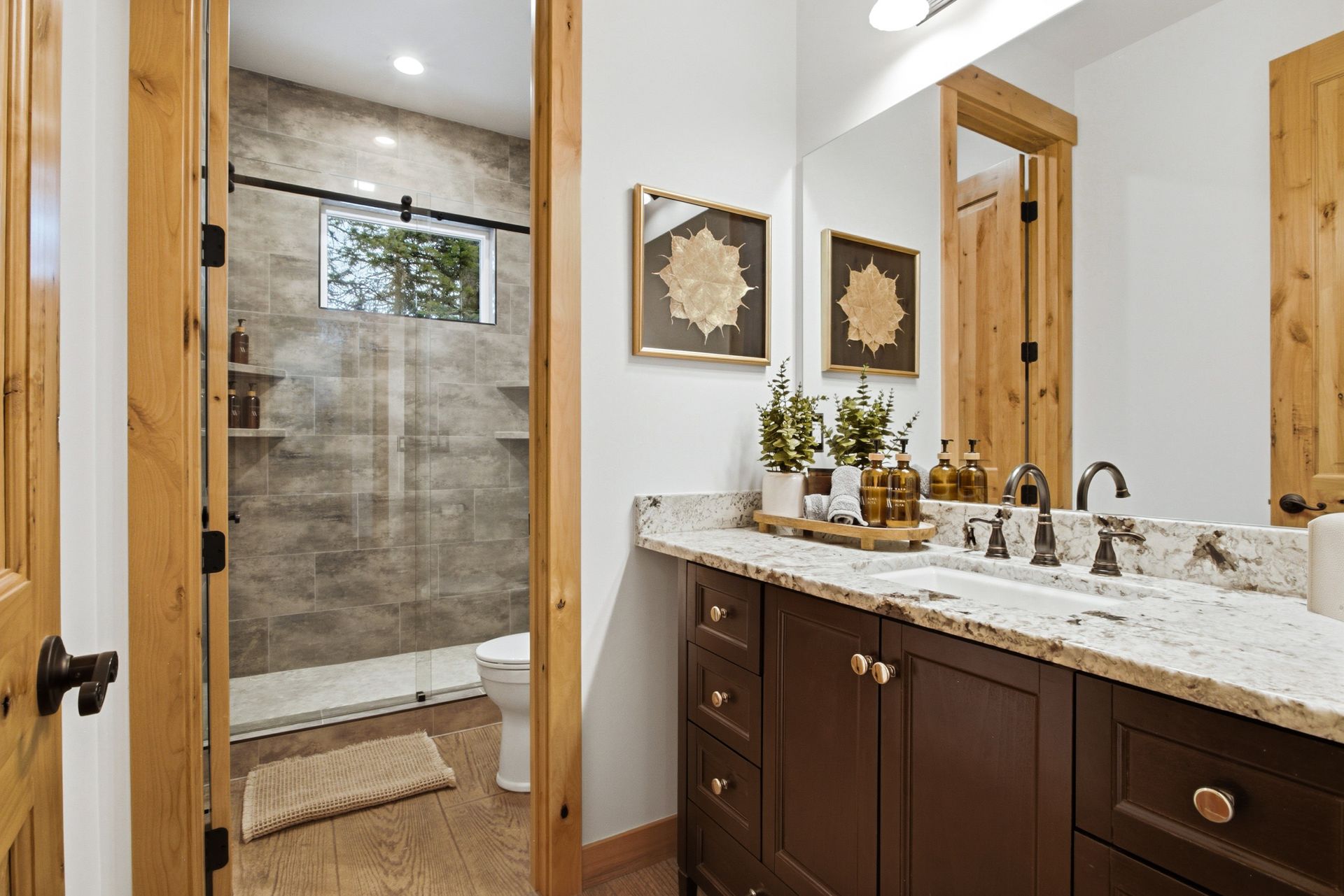 A modern bathroom featuring a dark wood vanity with a stone countertop, framed wall art, and an adjacent walk-in shower.