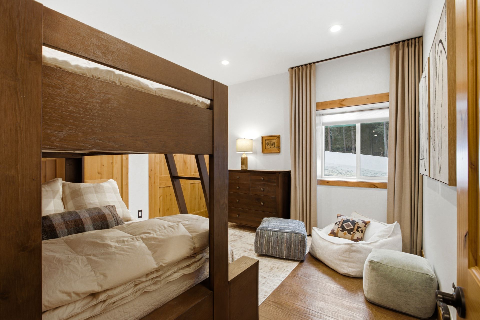 A wooden bunk bed, a wooden dresser, and lounge seating in a bright bedroom with floor-to-ceiling curtains.