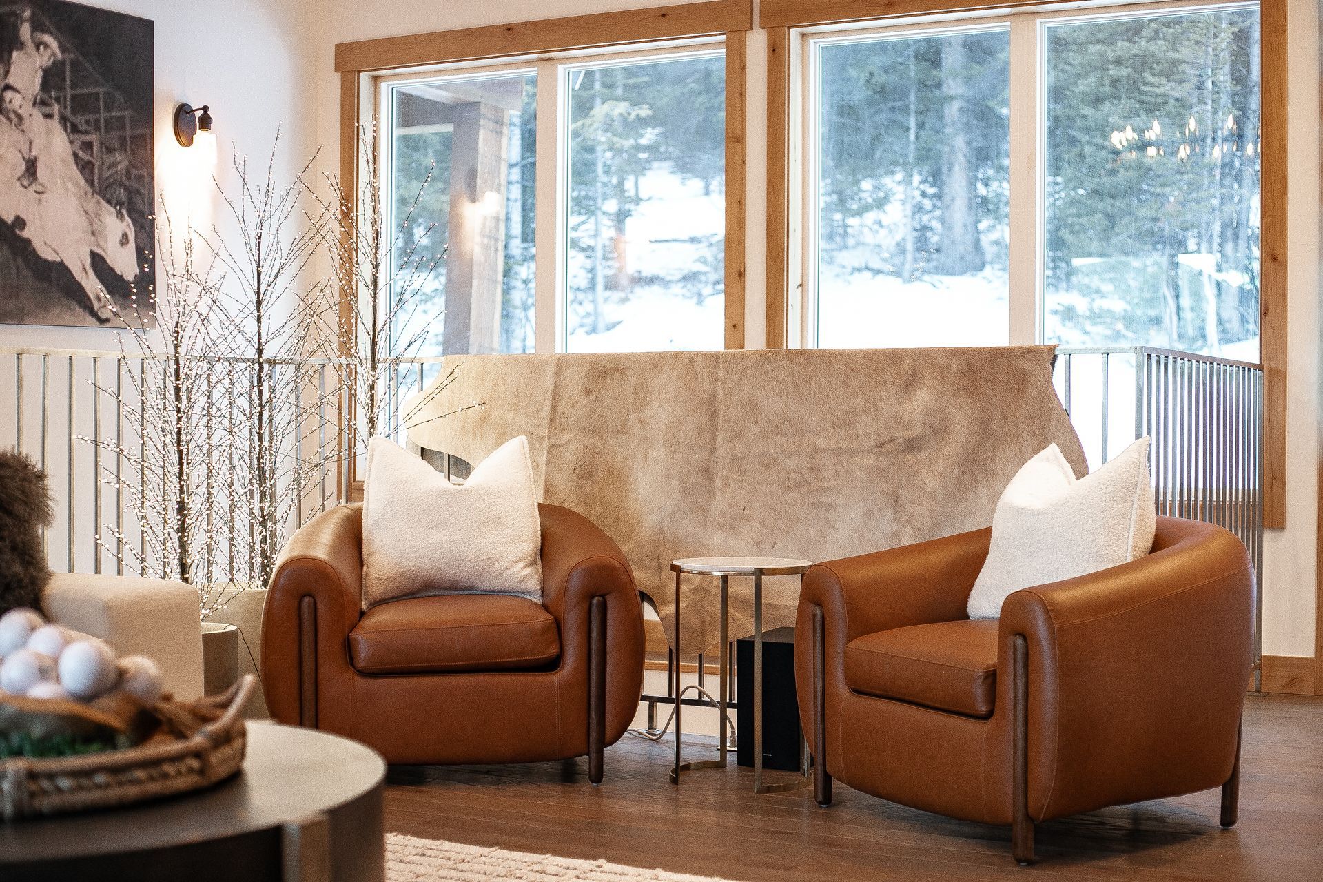 Two brown leather armchairs with white pillows face a window, with a small table between them in a living room.