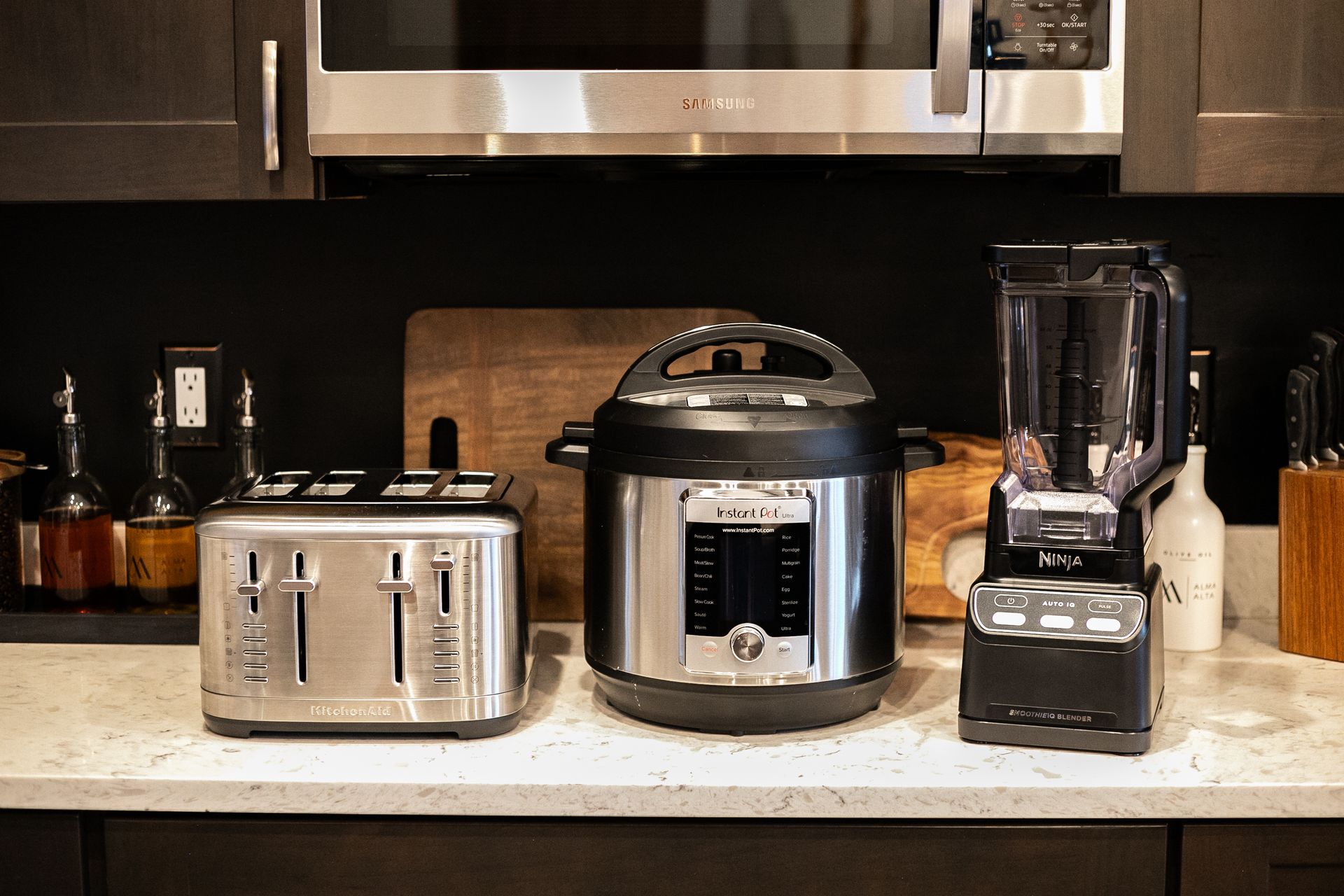 A stainless steel toaster, an Instant Pot, and a black blender sit on a kitchen counter beneath a microwave.