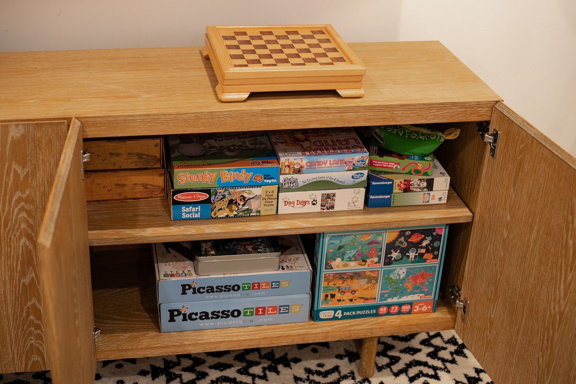 A wooden sideboard with an open cabinet, filled with board game boxes, topped with a small wooden chessboard.