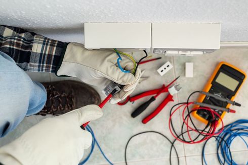 Un electricista está trabajando en una toma de corriente eléctrica con un par de alicates.