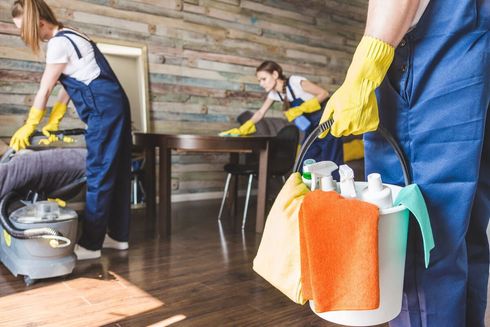 Un grupo de limpiadores está limpiando una habitación y una persona sostiene un balde con productos de limpieza.