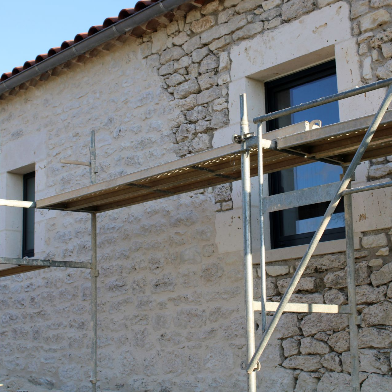 Façade en pierre d'un bâtiment en construction, avec échafaudages et fenêtres.
