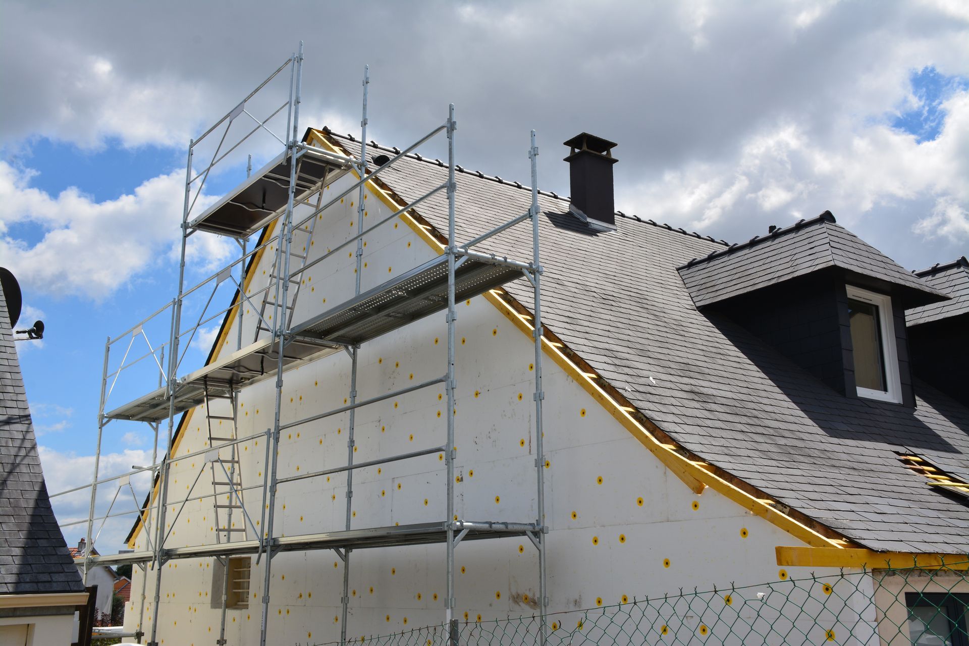 Échafaudages sur une maison en cours de rénovation extérieure ; panneaux isolants blancs et toit foncé.