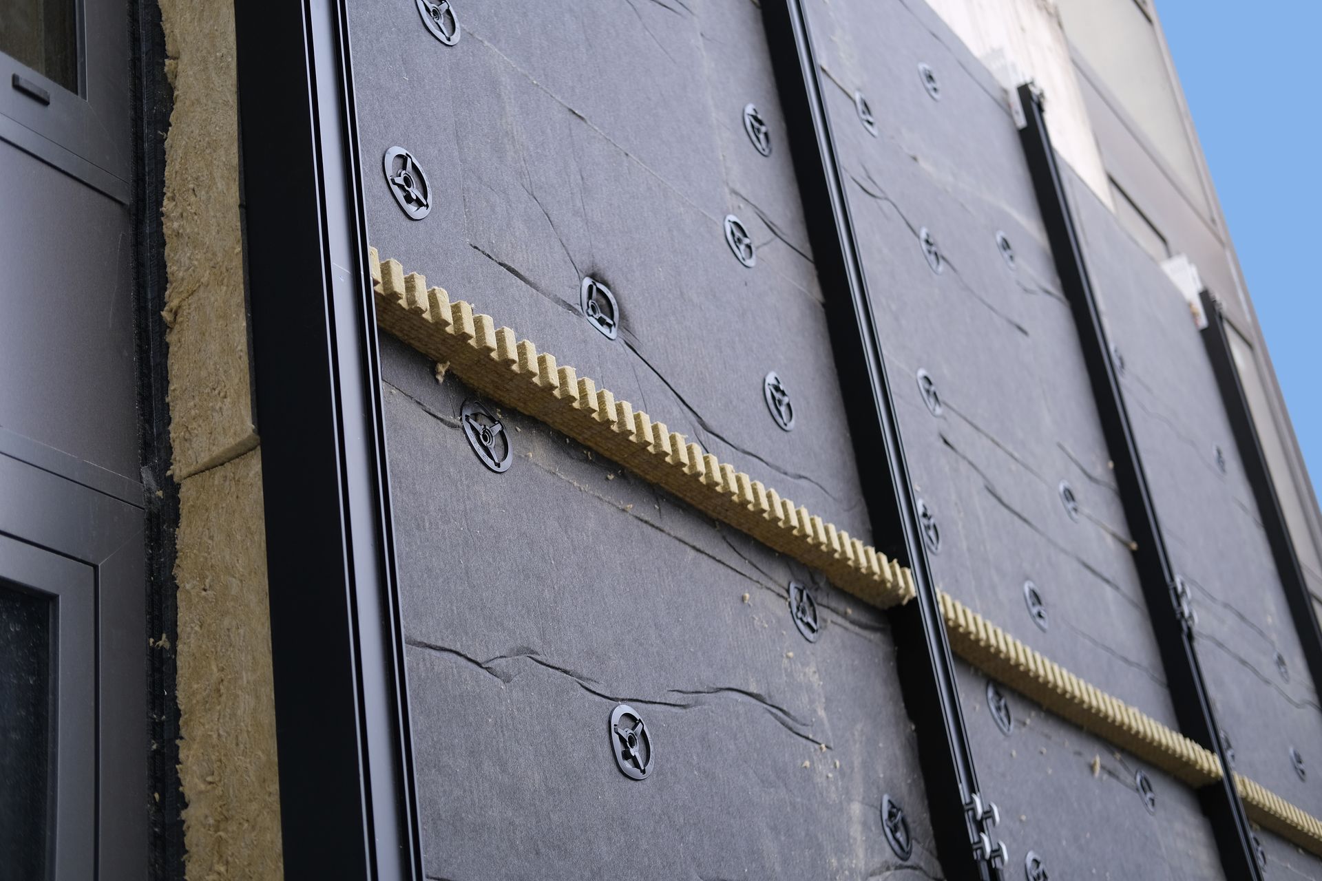 Construction des murs extérieurs : panneaux isolants noirs avec barres de support horizontales fixées au bâtiment.