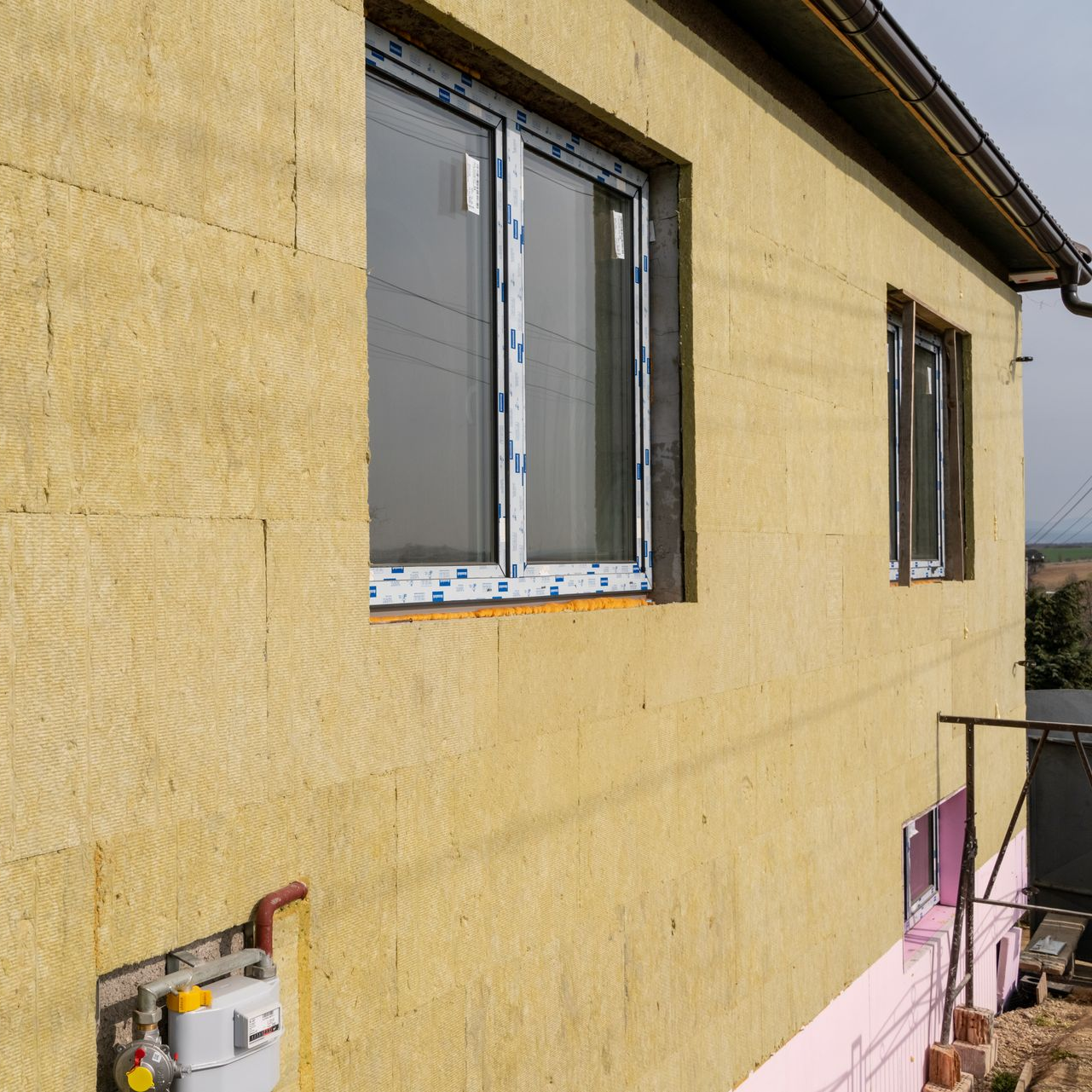 Mur extérieur d'un bâtiment en construction, avec isolation et encadrements de fenêtre. Matériau d'isolation jaune.
