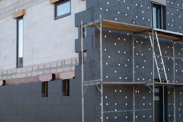 Extérieur d'un bâtiment en construction. Panneaux d'isolation sombres fixés aux murs, avec un échafaudage devant.