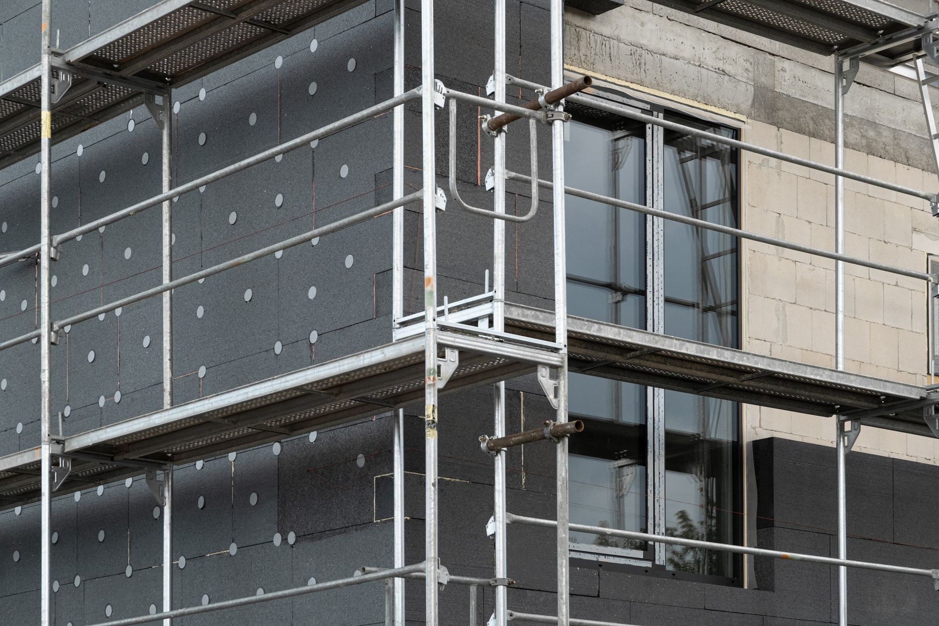 Extérieur d'un bâtiment en construction, avec échafaudages et panneaux d'isolation installés.