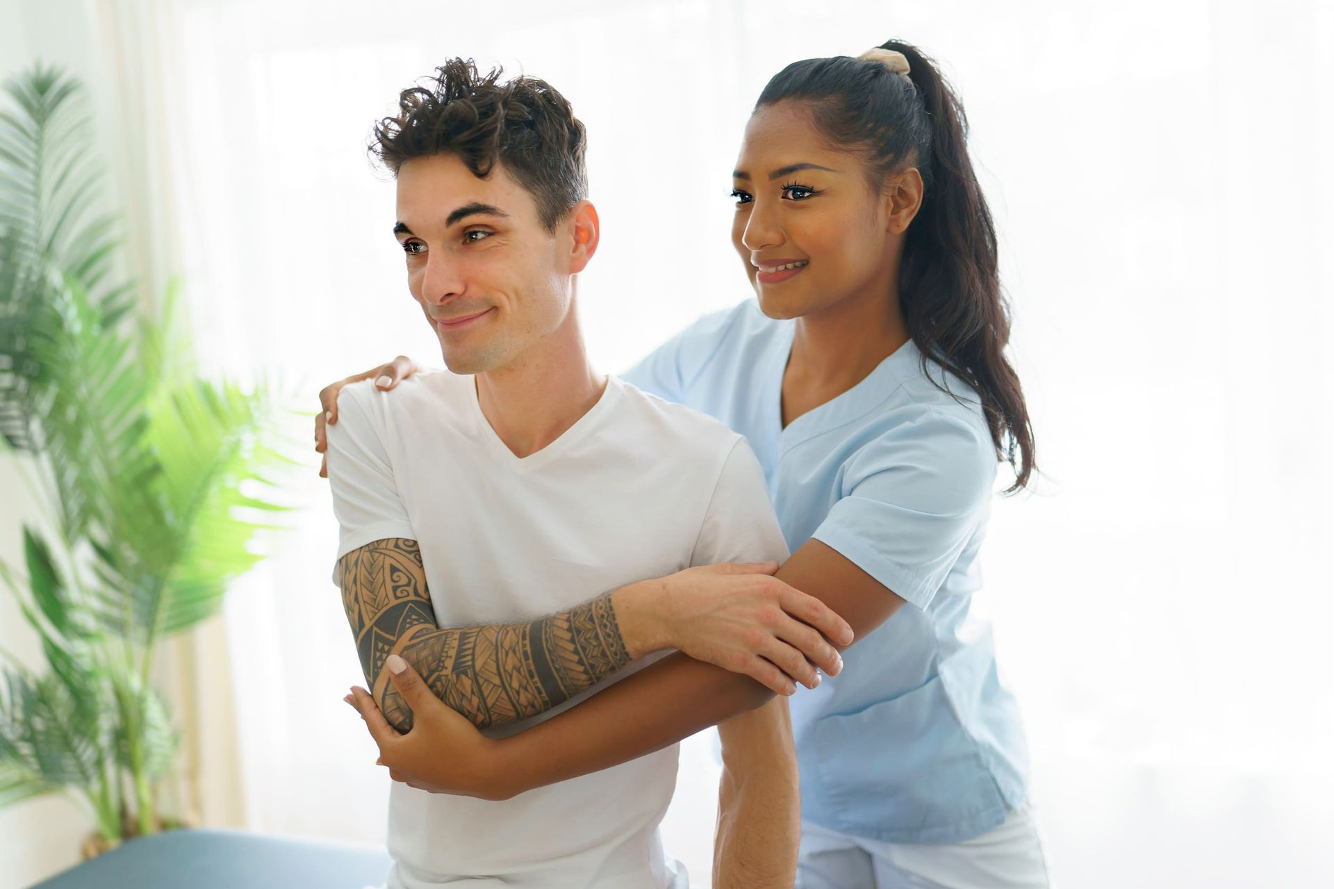 Mujer mayor con camisa rosa usando una banda de resistencia color verde azulado, asistida por las manos de otra persona para fisioterapia.