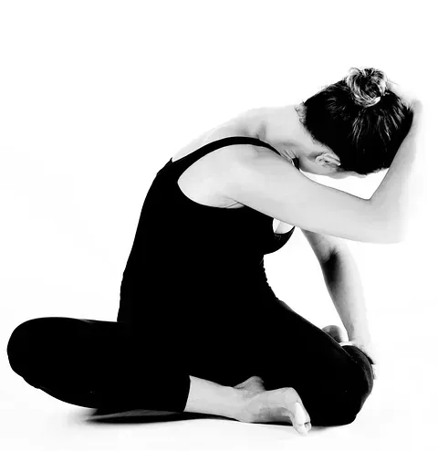 Mujer en leotardo negro sentada, con la cabeza inclinada hacia adelante, sosteniendo su cabeza con la mano derecha.