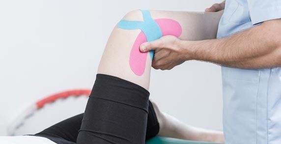 La rodilla de una persona con cinta kinesiológica siendo examinada por un profesional médico.