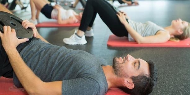Personas realizando ejercicios de puente de glúteos con placas de pesas en un gimnasio.