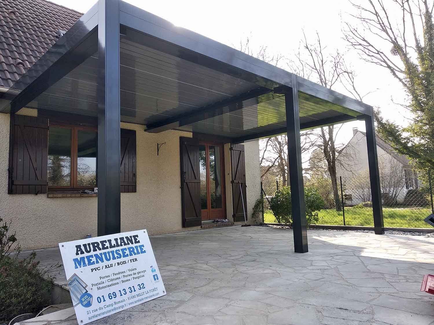 Pergola noir devant une maison avec la pancarte aurélianne menuserie