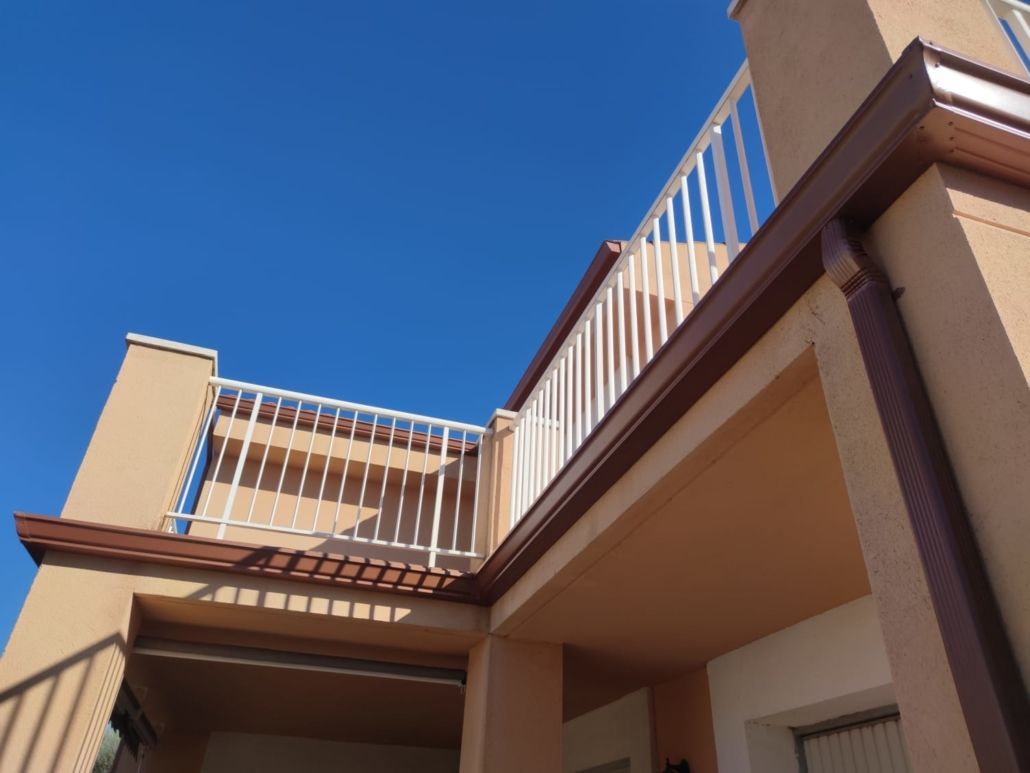 Vista desde un ángulo bajo del exterior de un edificio beige con barandillas blancas en dos niveles, contra un cielo azul despejado.