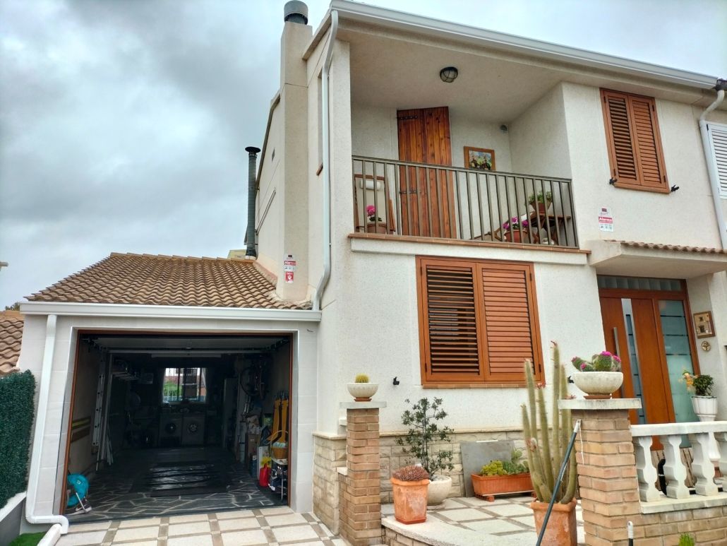 Una casa blanca de dos plantas con tejado de tejas, garaje abierto, balcón de madera y contraventanas marrones.