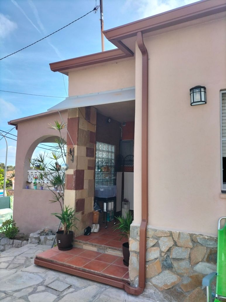 Una casa de color rosa claro con un porche delantero con detalles de piedra, una entrada de bloques de vidrio y un escalón con baldosas de terracota.