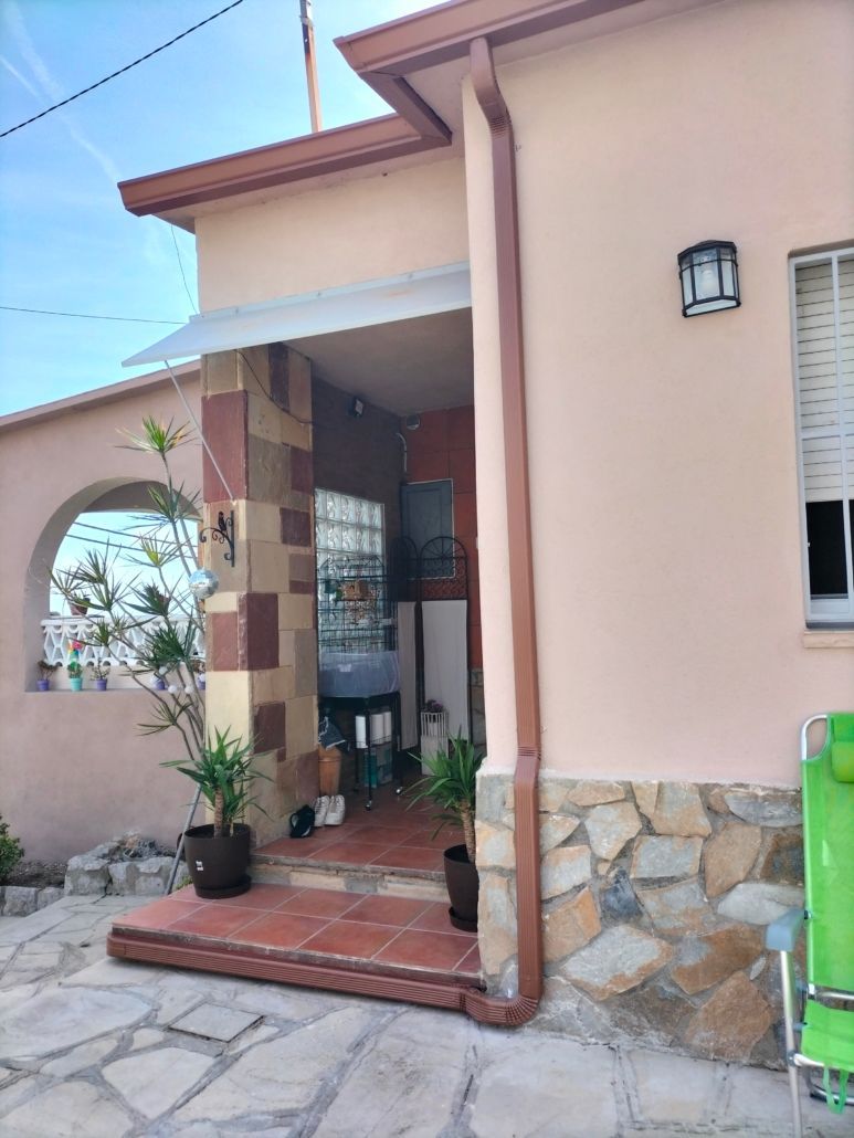 Una entrada a la casa de color melocotón con un pilar adornado con piedra, escaleras de baldosas rojas, una puerta de bloques de vidrio y plantas en macetas.