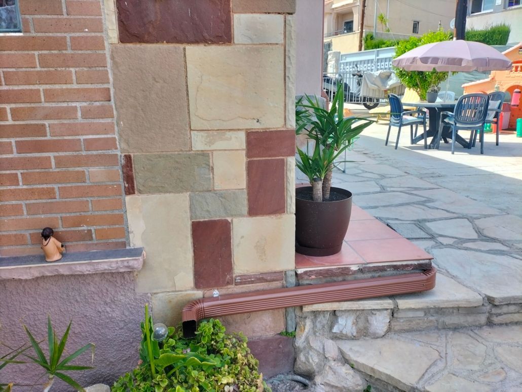Al fondo se aprecia un muro de ladrillo y piedra, una pequeña figurita decorativa sobre una repisa, una planta en maceta y un conjunto de muebles de patio.