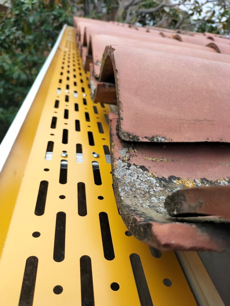 Un protector de canalón de metal amarillo instalado a lo largo del borde de un tejado de tejas de arcilla.