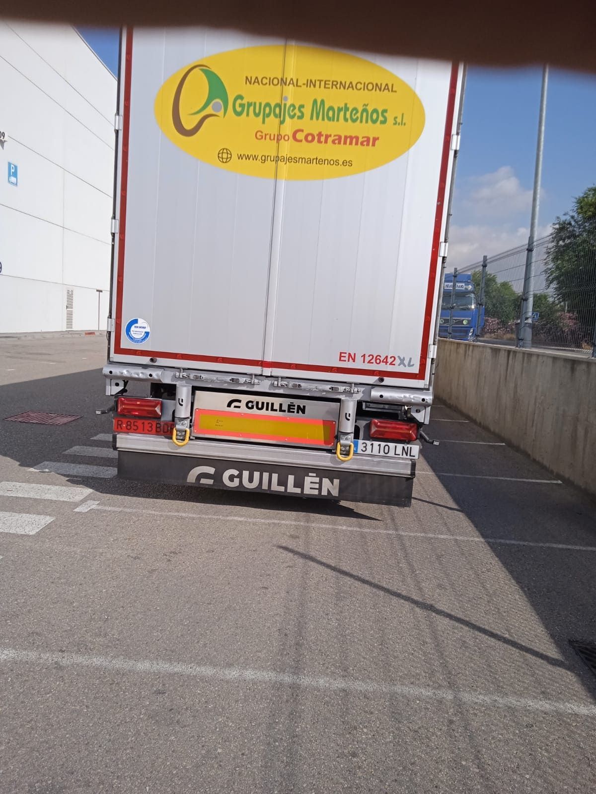 Vista trasera de un camión semirremolque blanco estacionado en un aparcamiento pavimentado, con el logotipo amarillo de "Grupajes Martiños" y Guillén.