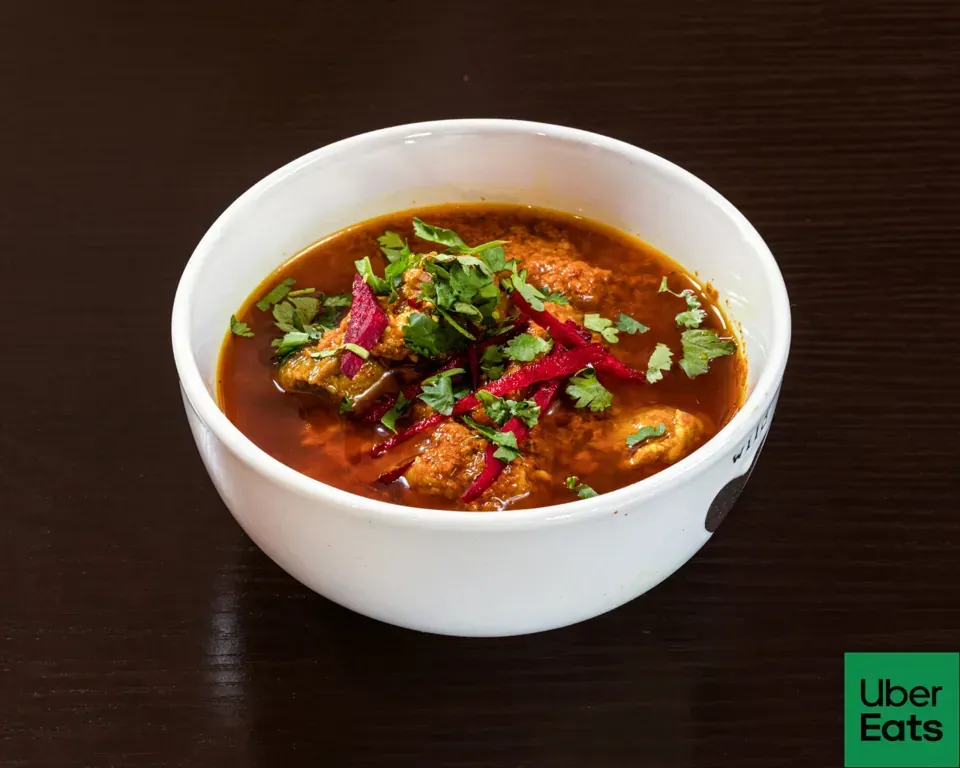 Tazón de curry rojizo con trozos de carne, pimientos rojos y cilantro sobre una mesa de madera oscura.