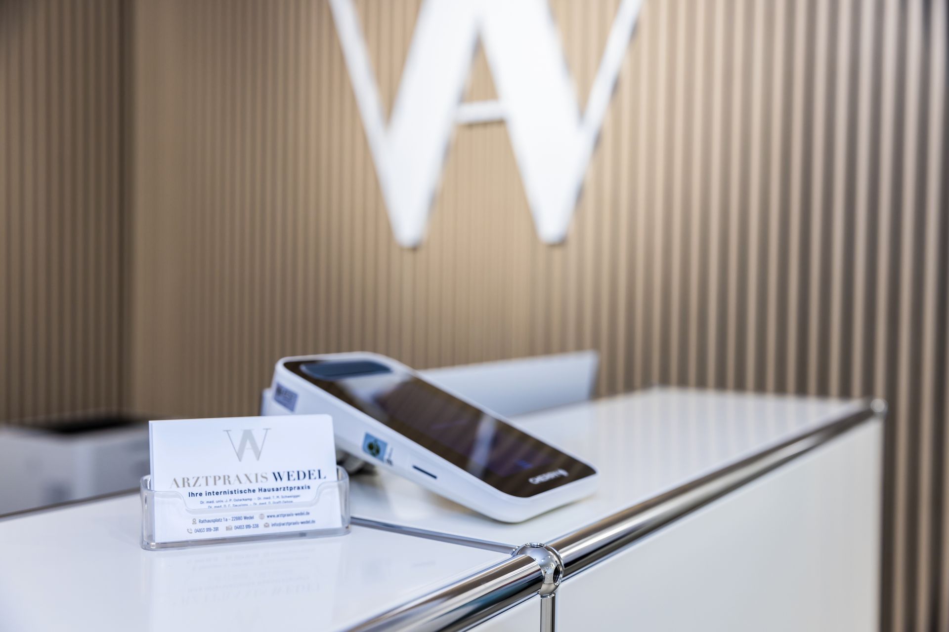Rezeption mit Zahlungsterminal und Visitenkarte, unter einem weißen „W“-Logo.