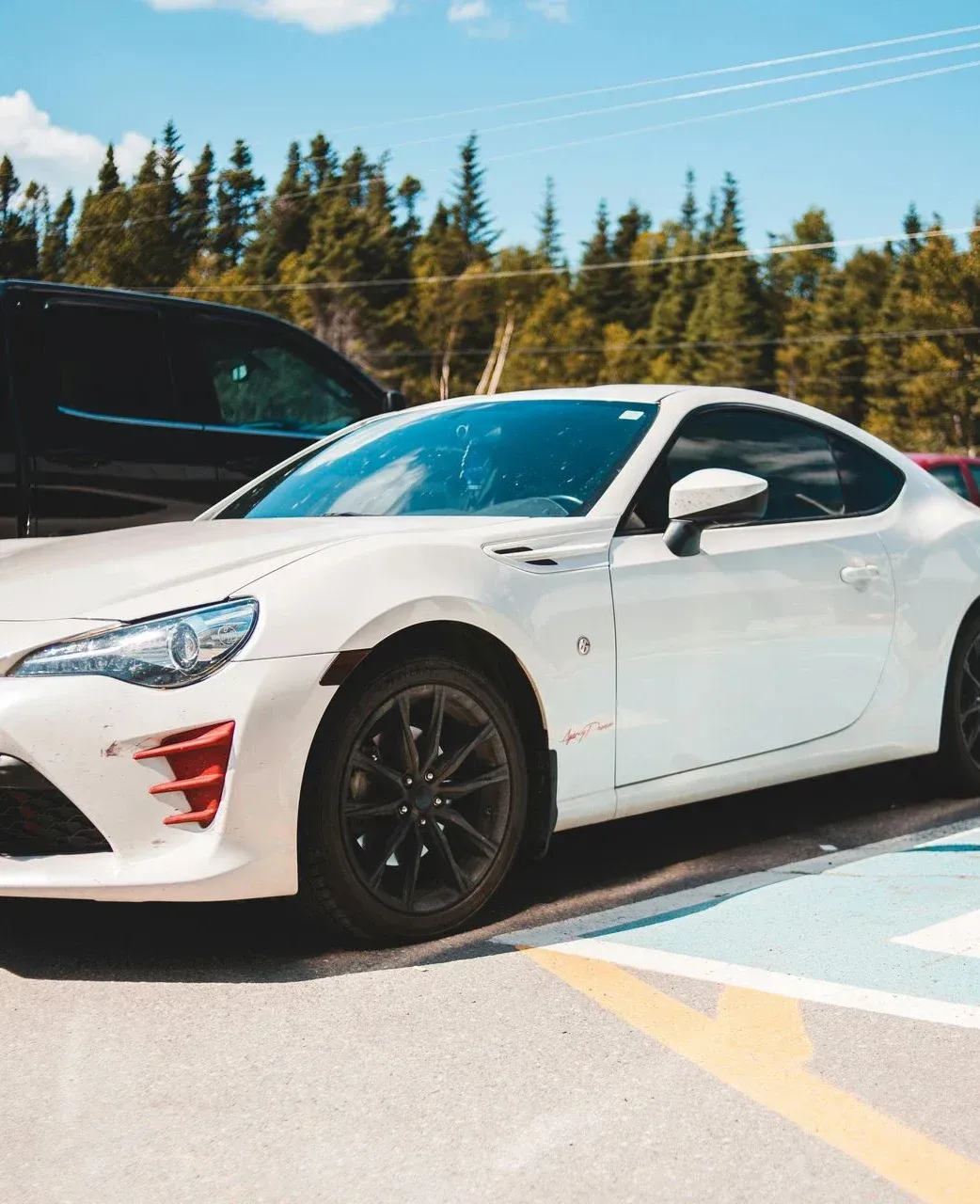 Coche deportivo blanco aparcado sobre una superficie pintada de azul y blanca con un bosque de fondo.