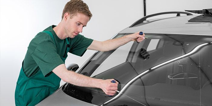 Une personne portant une salopette verte nettoie le pare-brise d'une voiture avec un outil.