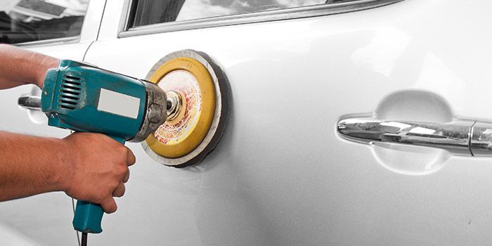 Personne utilisant une polisseuse électrique pour polir une portière de voiture blanche.