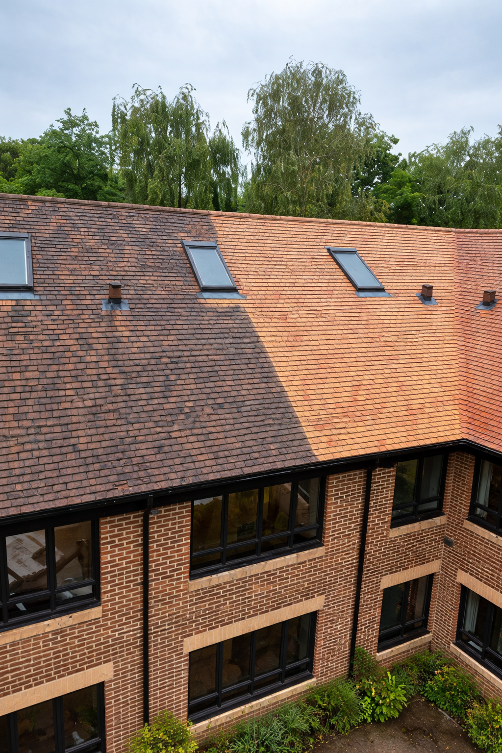 Brick apartment building with sloped tiled roof and skylight windows under a partly cloudy sky